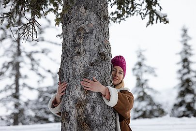 Frau umarmt Baum in Schneelandschaft