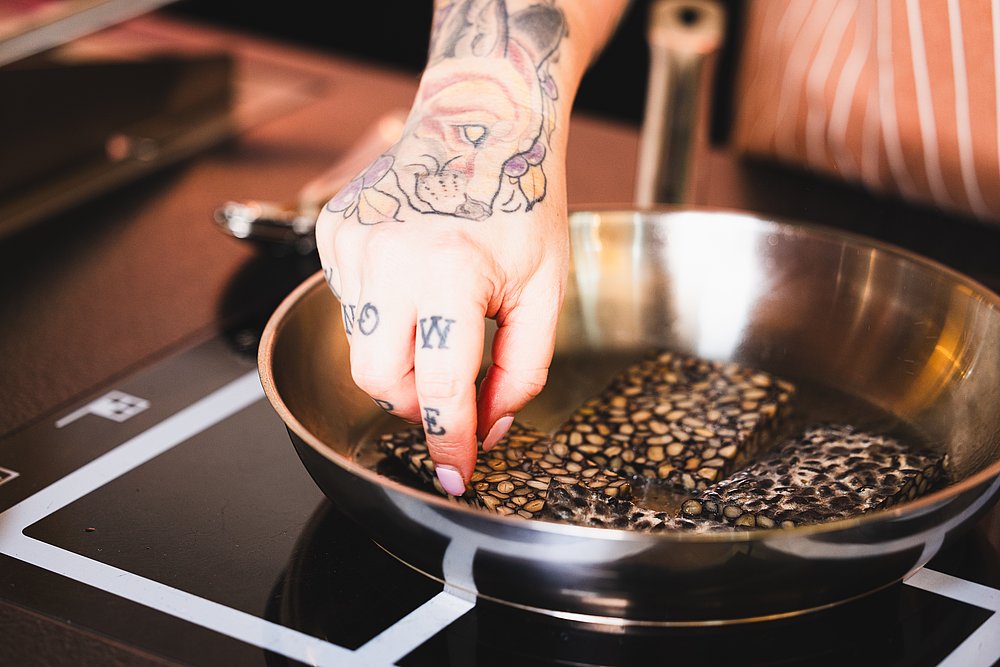 Tätowierte Hand wendet Tempeh in einer Pfanne