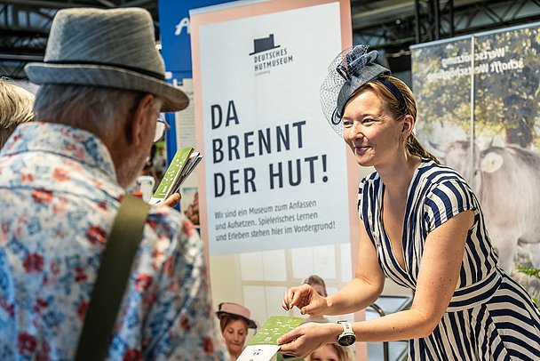 Frau mit Hut reicht einem Mann einen Flyer