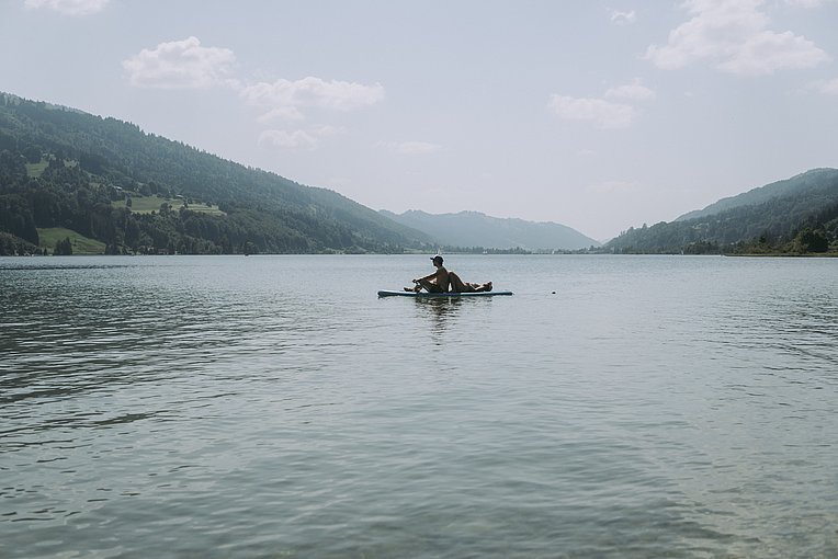 Zwei Personen auf einem SUP auf dem Großen Alpsee mit Bergen am Ufer