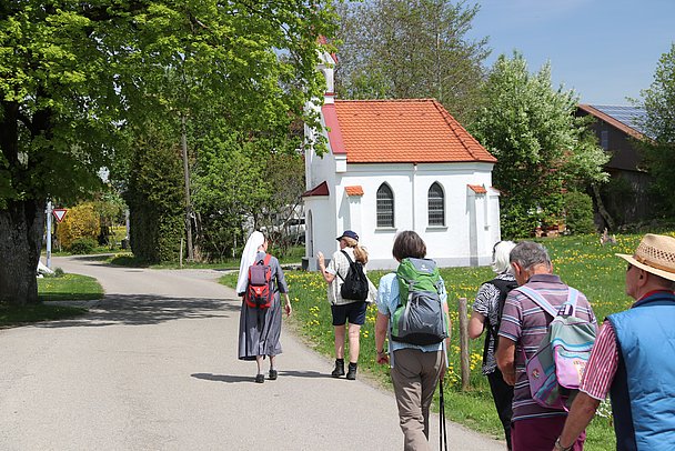 Pilgergruppe geführt von einer Nonne wandert an einer Kapelle vorbei
