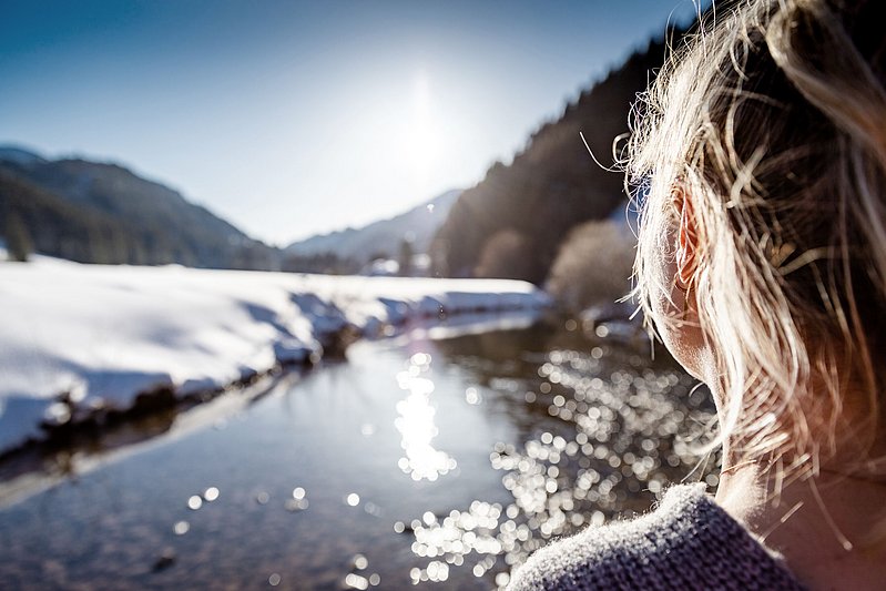 Frau steht mit dem Rücken zur Kamera und blick im Winter in die Sonne Frau steht mit dem Rücken zur Kamera und blick im Winter in die Sonne