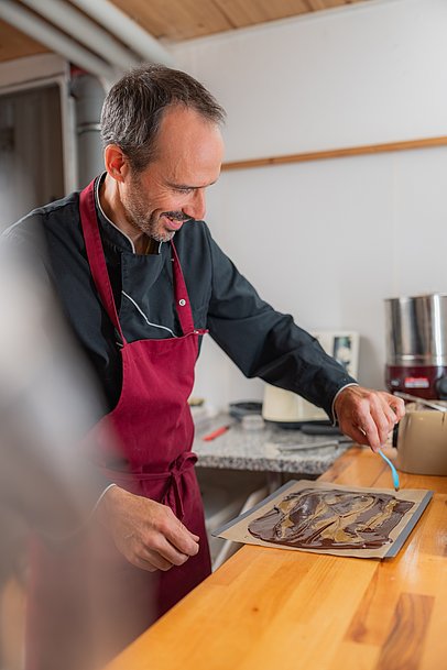 Chocolatier Jonathan Baldinger streicht mit einem Löffel Muster in flüssige Schokolade