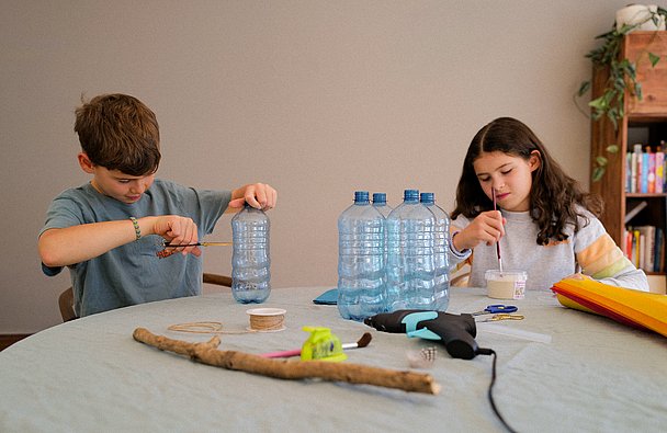 Fackel basteln: Junge und Mädchen schneiden Wasserflaschen auseinander und rühren Bastelkleber an 