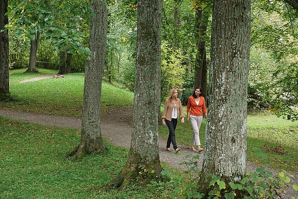 Im Vordergrund ein Schild mit einem Zitat von Kneipp, im Hintergrund zwei Frauen beim Spazieren im Park