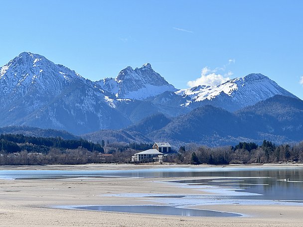 Leerer Forggensee mit Pfützen und verschneiten Bergen