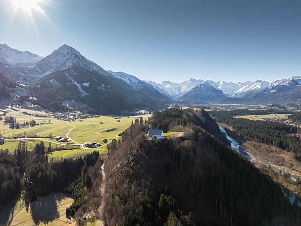 Schöllanger Burgkirche auf einem bewaldeten Hügel, im Hintergrund verschneite Berge Schöllanger Burgkirche auf einem bewaldeten Hügel, im Hintergrund verschneite Berge