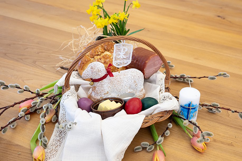Osterkorb mit gebackenem Osterlamm, bunten Eiern, Butter, Salz, Osterbrot und Schinken