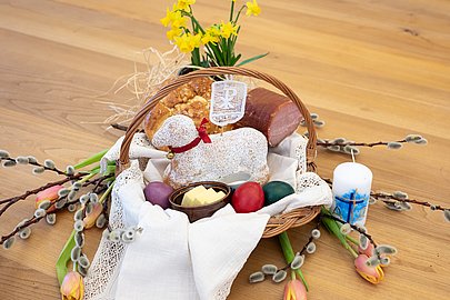 Osterkorb mit gebackenem Osterlamm, bunten Eiern, Butter, Salz, Osterbrot und Schinken