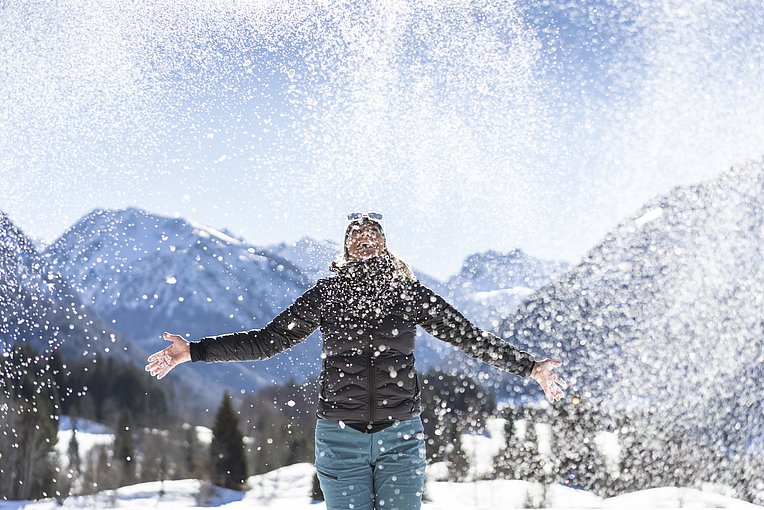 Frau vor Bergpanorama schmeißt Schnee in die Luft