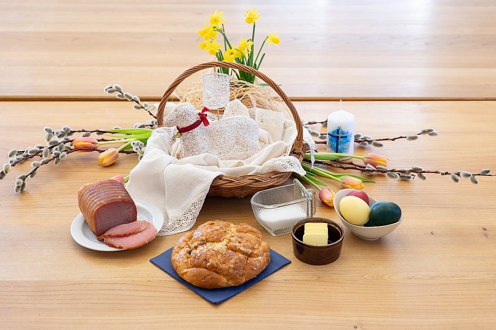 Osterkorb mit gebackenem Osterlamm, bunten Eiern, Butter, Salz, Osterbrot und Schinken