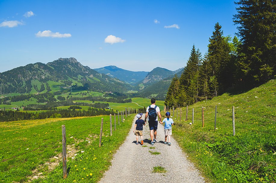 Frau wandert mit zwei Kindern auf einem Wanderweg im Allgäu mit Bergpanorama im Hintergrund