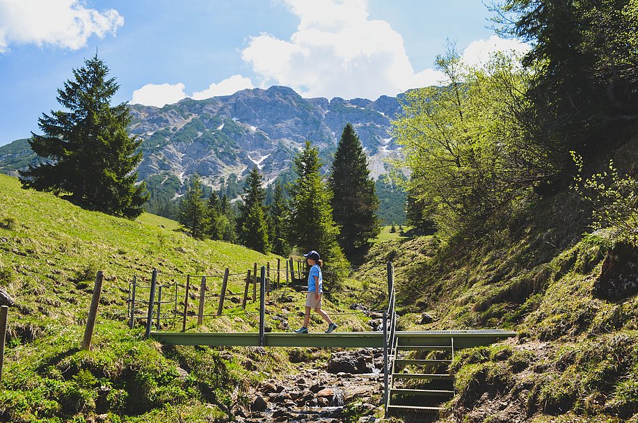 Mädchen wandert auf einer kleinen Holzbrücke in der Natur mit Bergpanorama im Hintergrund