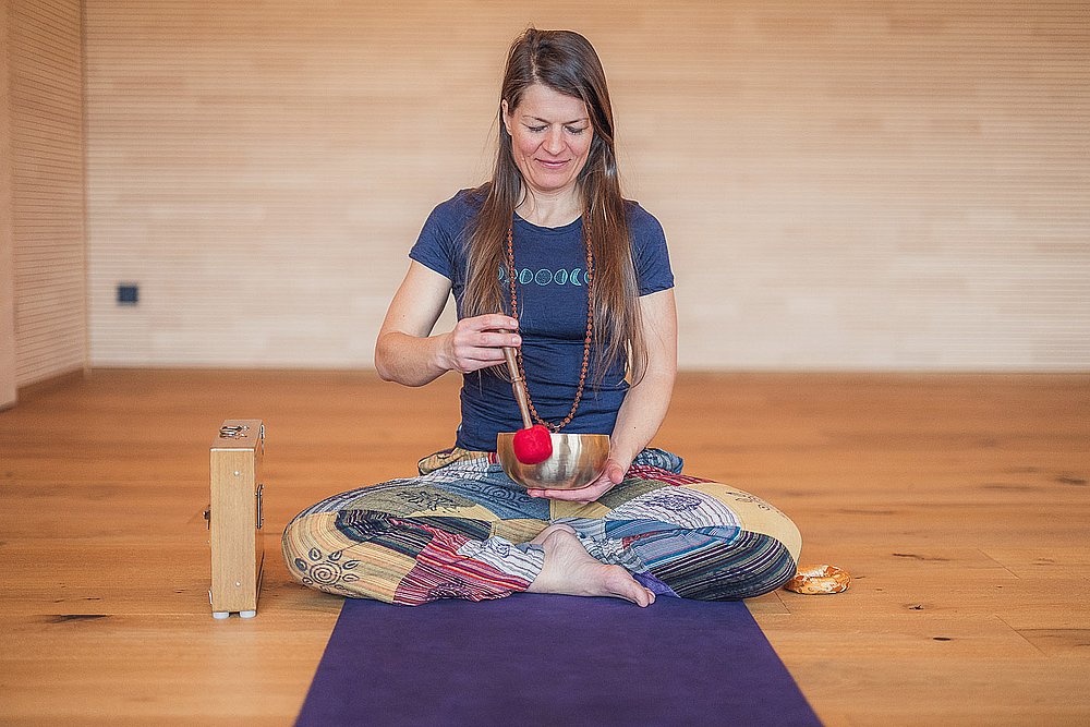 Frau im Schneidersitz auf einer Yogamatte mit Klangschale