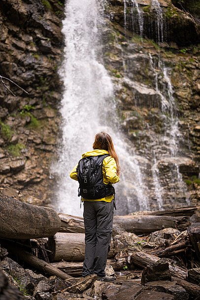 Frau mit Rucksack von hinten vor einem Wasserfall