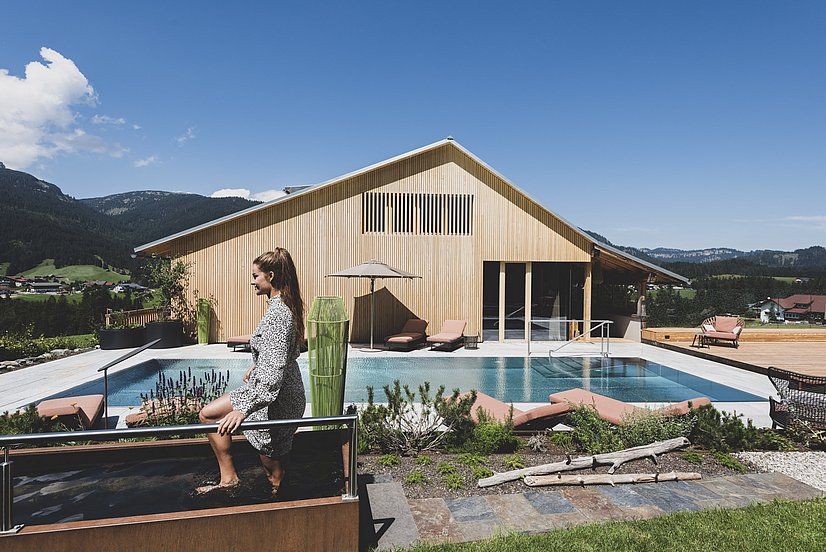 Hotel mit Holzfassade, Außenpool und Frau im Kneipp-Becken