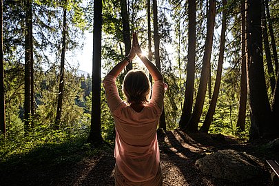 Frau von hinten im Wald, die Hände über dem Kopf zusammengelegt