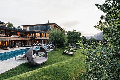 Naturhotel Chesa Valisa, Holzfassade,davor Pool, Wiese und im Hintergrund Berge