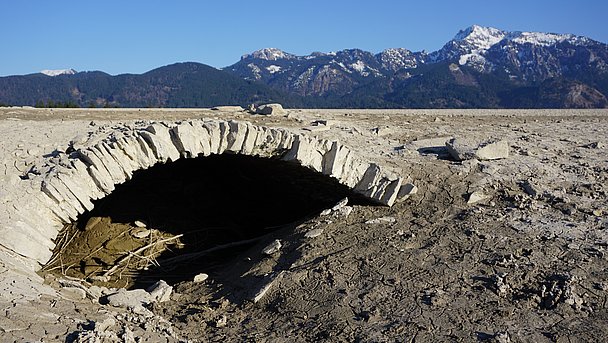 Leerer Forggensee vor verschneiten Bergen