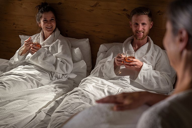 Mann und Frau im Bademantel lächelnd im Bett, Tee in der Hand