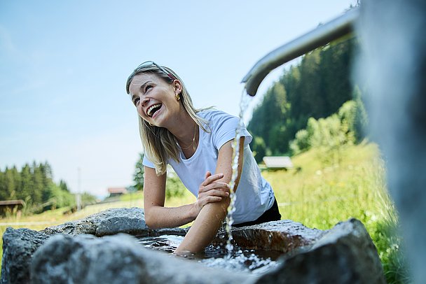 Lachende Frau kühlt Arme in einem Kneipp-Becken