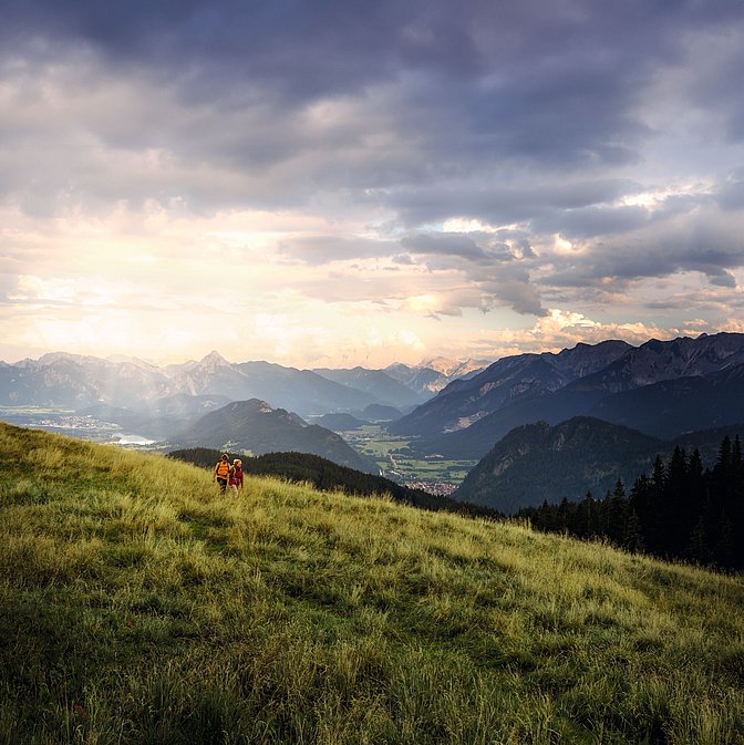 Zwei Wanderer auf einem Wiesenhügel, im Hintergrund die Allgäuer Alpen