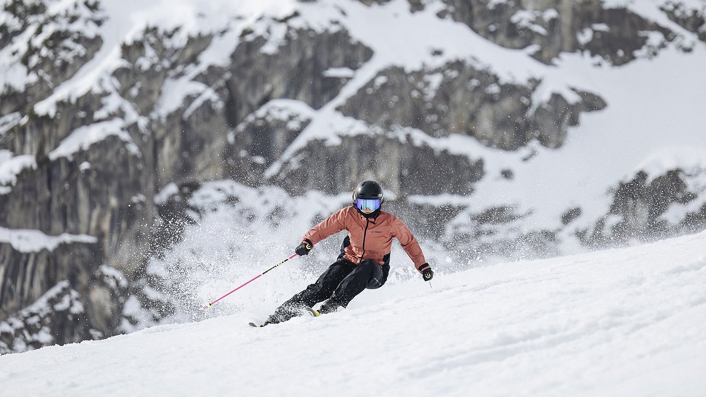 Eine Skifahrerin bei einer schnellen Abfahrt, im Hintergrund eine Felswand