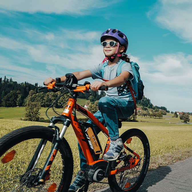 Kind fährt mit Fahrrad auf Weg zwischen grünen Wiesen