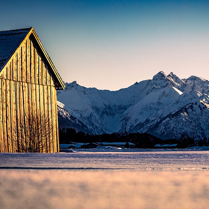 Winterliche Berge und eine Holzhütte, die im Licht der untergehenden Sonne erstrahlt