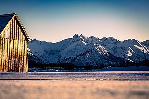 Winterliche Berge und eine Holzhütte, die im Licht der untergehenden Sonne erstrahlt