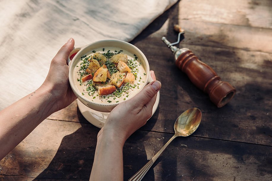 Zwei Hände stellen eine frische Allgäuer Käsesuppe auf einen Tisch