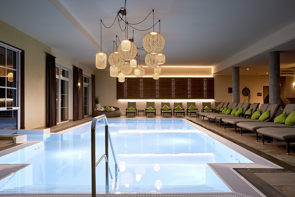 Pool im Panoramahotel Oberjoch mit stimmungsvoller Beleuchtung und Liegestühlen