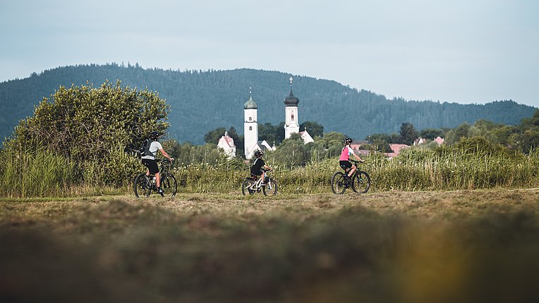 Familie auf Rädern fährt über einen Wiese, im Hintergrund die Türme Isnys