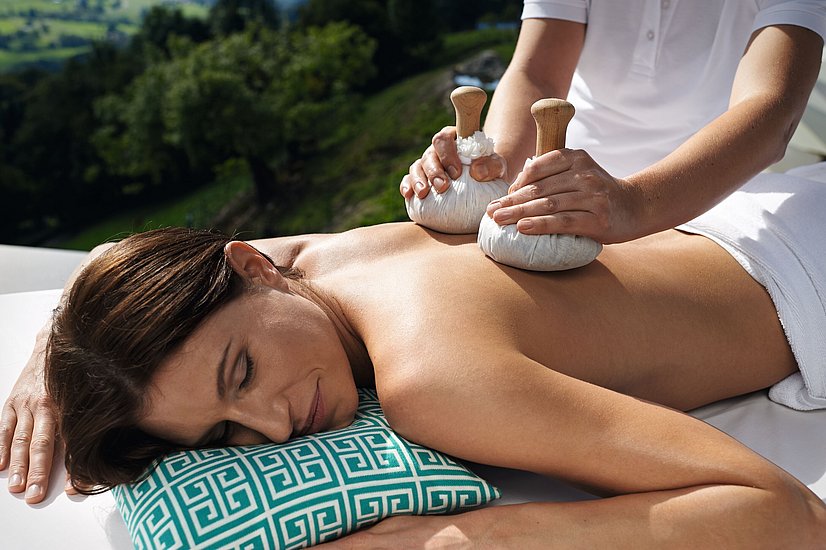 Frau auf einer Liege bekommt draußen eine Massage mit Kräuterstempeln