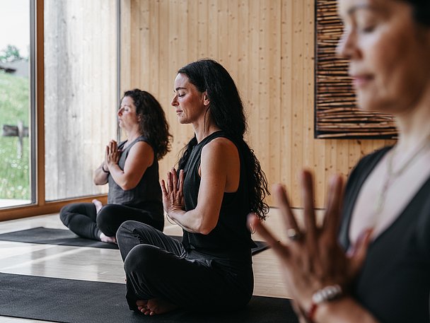 Frauen im Schneidersitz mit geschlossenen Augen in einem Yogaraum