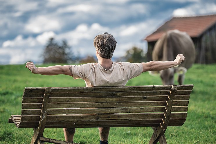 Mann sitzt mit ausgebreiteten Armen auf einer Bank