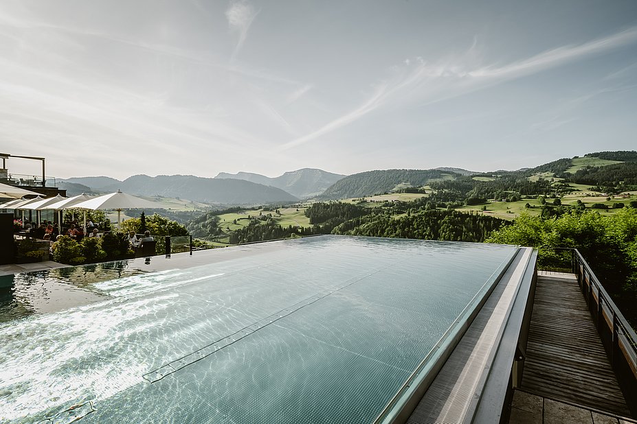 Infinitypool mit Blick in die Berge, daneben eine Terrasse mit Sonnenschirmen