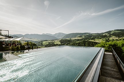 Infinitypool mit Blick in die Berge, daneben eine Terrasse mit Sonnenschirmen