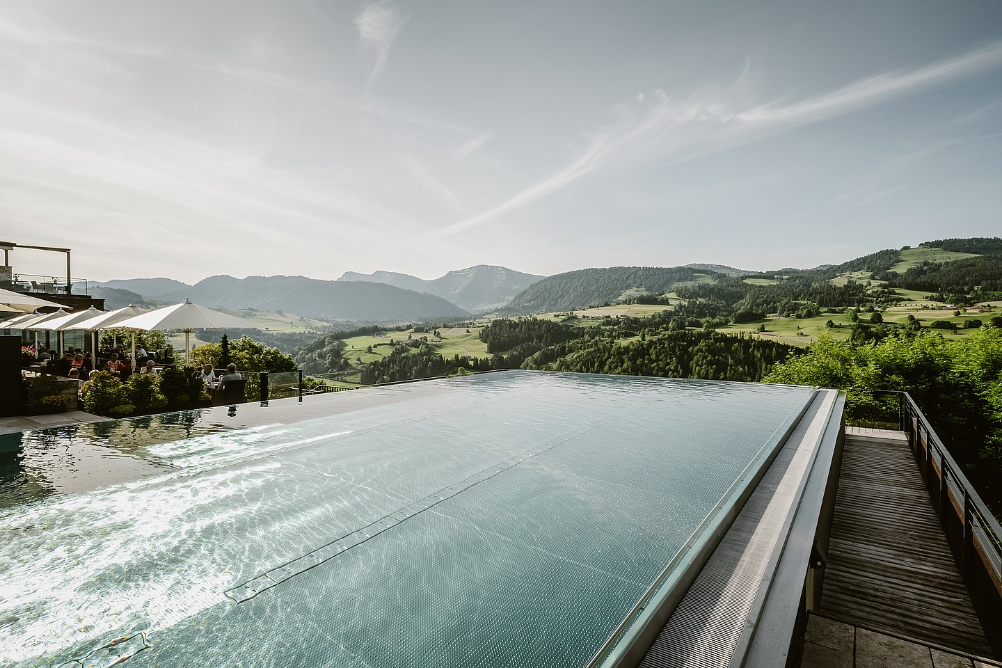 Infinitypool mit Blick in die Berge, daneben eine Terrasse mit Sonnenschirmen