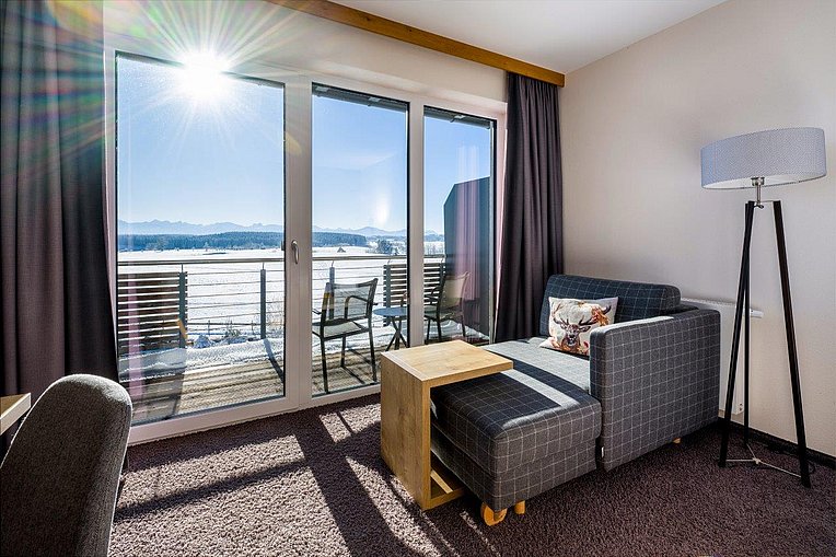 Hotelzimmer im Das Weitblick mit Sofa und Balkon mit Blick über die Schneelandschaft bis zur Alpenkette