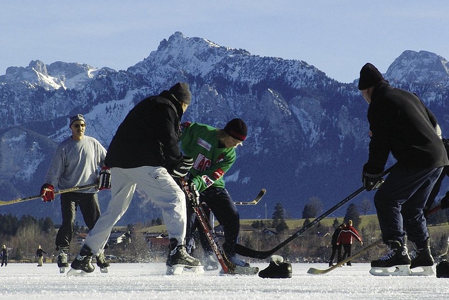 Eishockeyspieler auf einem zugefrorenen See, im Hintergrund die Berge