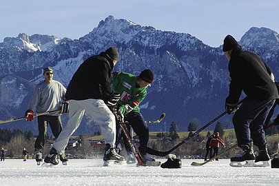 Eishockeyspieler auf einem zugefrorenen See, im Hintergrund die Berge