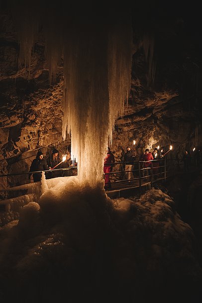 Beleuchteter gefrorener Wasserfall in der Breitachklamm, Wandergruppe mit Fackeln Beleuchteter gefrorener Wasserfall in der Breitachklamm, Wandergruppe mit Fackeln