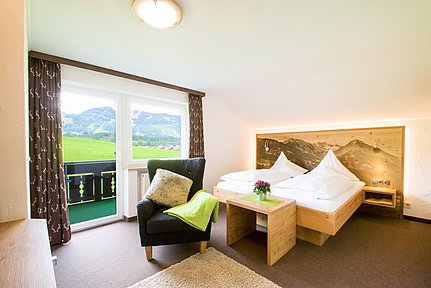 Zimmer im Hotel Alpenblick in Fischen mit Bett, Sessel und Balkon mit Blick auf die Berge
