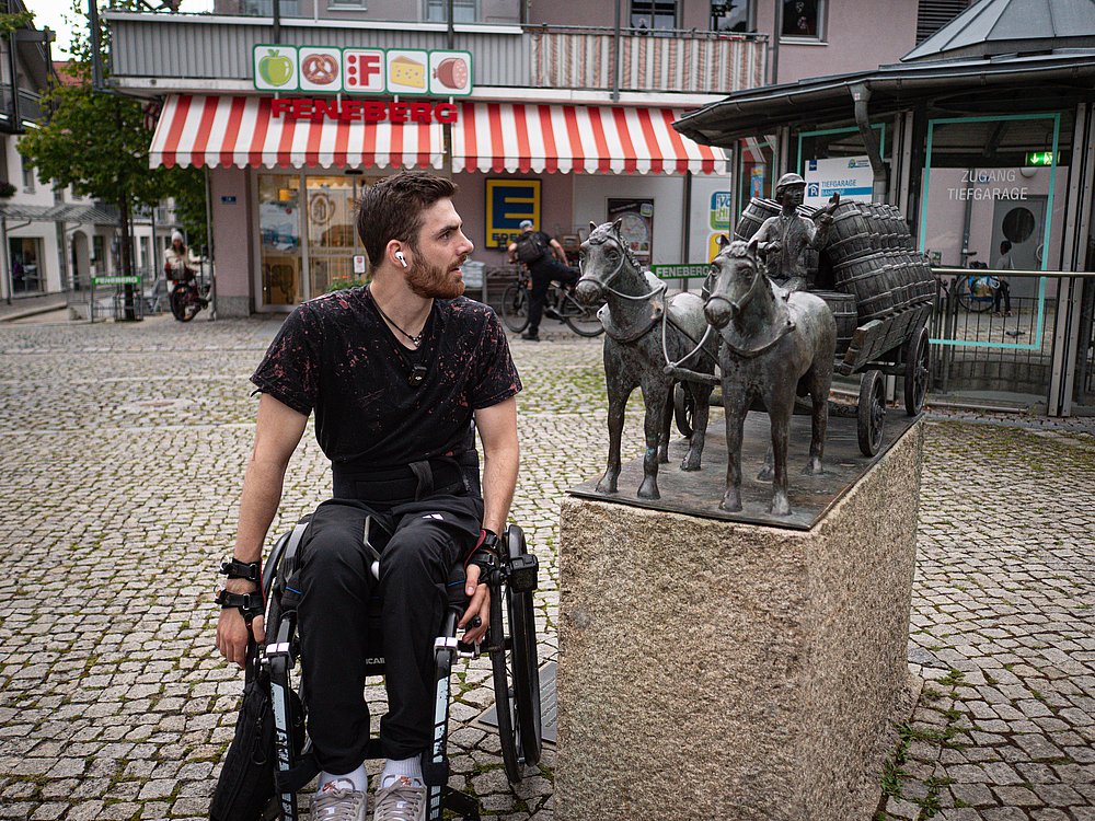 Moritz Brückner im Rollstuhl neben einer Skulptur eines Pferdegespanns mit Fässern auf der Kutsche