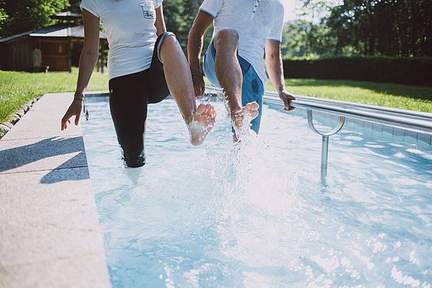 Zwei Menschen in einem Kneipp-Becken, spritzen mit den Füßen im Wasser