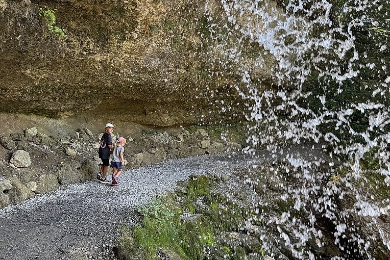 Zwei Kinder gehen hinter einem Wasserfall entlang