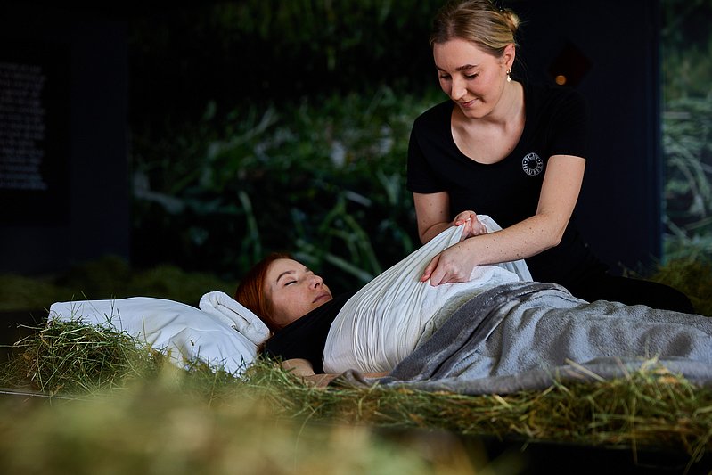 Eine Frau deckt eine Frau zu, die in einem Heubett liegt