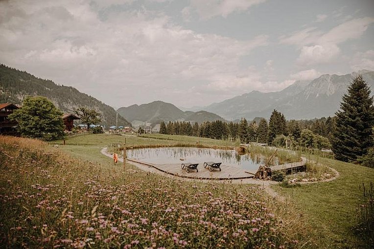 Naturteich mit Sonnenliegen und Bergblick auf der Alpe Dorach