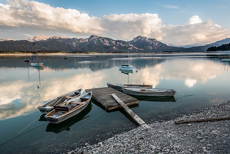 Ruderboote liegen an einer schwimmenden Plattform im Forggensee, im Hintergrund die Berge Ruderboote liegen an einer schwimmenden Plattform im Forggensee, im Hintergrund die Berge